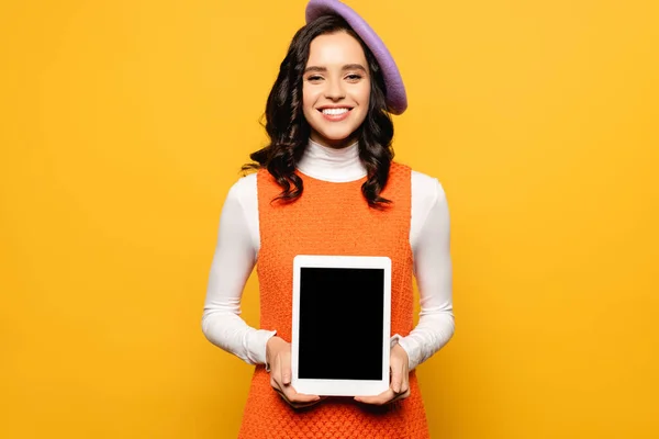 Front view of happy brunette woman in beret looking at camera while holding digital tablet isolated on yellow — Stock Photo