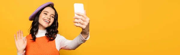 Happy woman with waving hand, wearing beret and taking selfie isolated on yellow, banner — Stock Photo