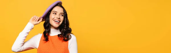 Happy brunette woman laughing and touching beret while looking away isolated on yellow, banner — Stock Photo