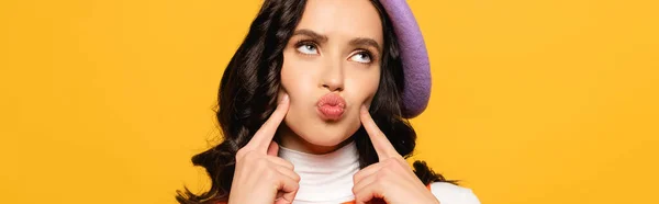 Brunette woman in beret with pouting lips looking up isolated on yellow, banner — Stock Photo