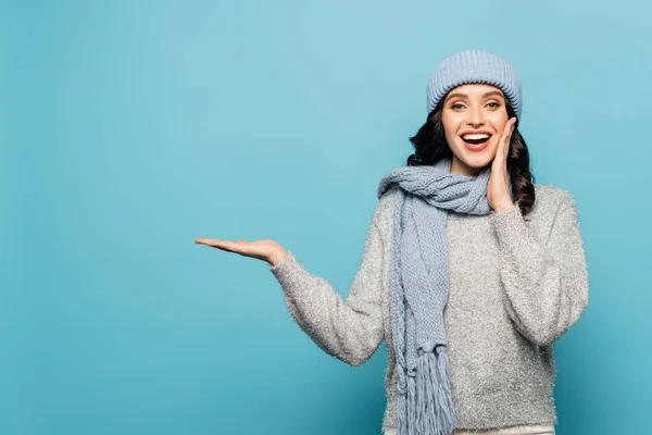 Front view of excited woman with open mouth, wearing winter outfit and pointing with hand isolated on blue — Stock Photo