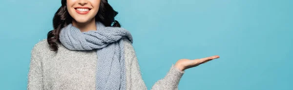 Vista recortada de mujer morena en bufanda apuntando con la mano aislada en azul, pancarta — Stock Photo