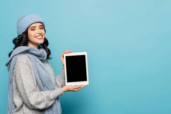 Cheerful brunette woman in winter outfit showing digital tablet with blank screen isolated on blue — Stock Photo