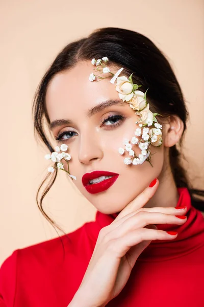 Junge Frau mit roten Lippen und Blumen im Gesicht, die isoliert auf rosa Kamera schaut — Stockfoto