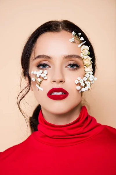 Brünette Frau mit roten Lippen und Blumen im Gesicht, die vereinzelt in die Kamera auf rosa schaut — Stockfoto