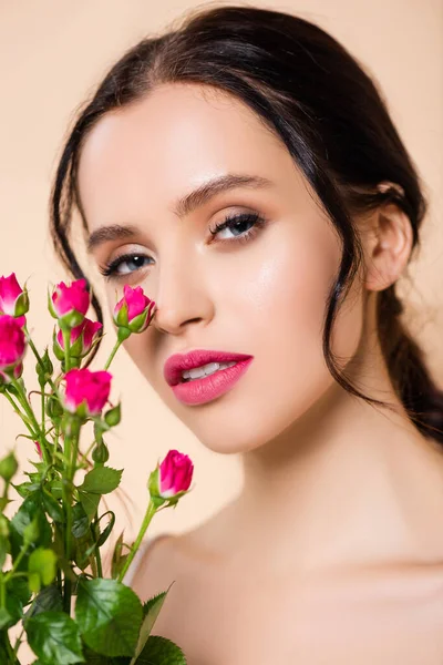 Mujer joven mirando a la cámara cerca de flores aisladas en rosa - foto de stock