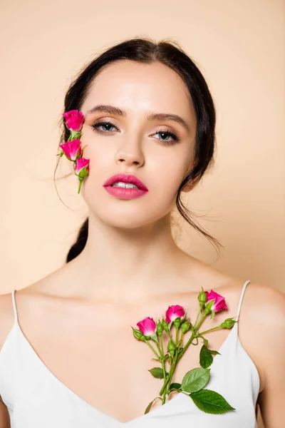 Sensual jovem mulher olhando para a câmera perto de flores isoladas em rosa — Fotografia de Stock