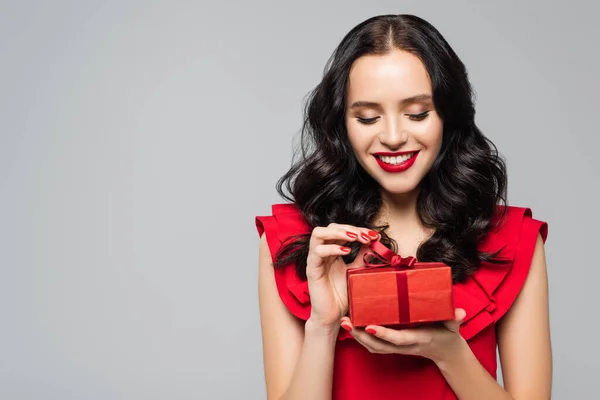 Fröhliche Frau im Rüschenkleid zieht Schleife auf Geschenkbox isoliert auf grau — Stockfoto