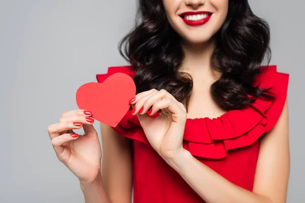 Обрізаний вид веселої молодої жінки, що тримає червоне паперове серце ізольовано на сірому — стокове фото
