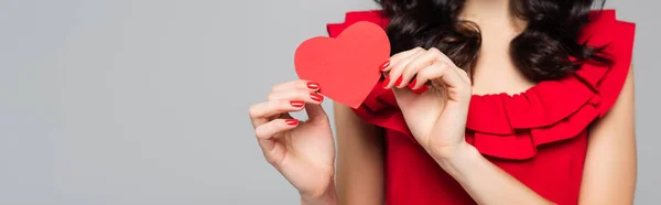 Vue recadrée d'une jeune femme tenant un cœur en papier rouge isolé sur du gris, bannière — Photo de stock