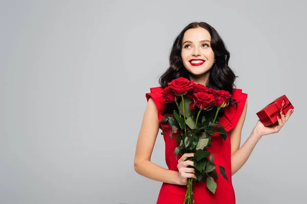 Pleased woman holding roses and wrapped box isolated on grey — Stock Photo