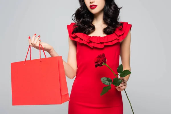 Обрізаний вид жінки, що тримає торгову сумку і троянду ізольовано на сірому — стокове фото