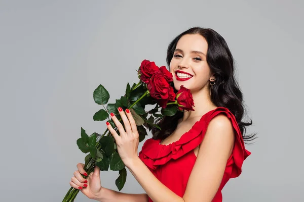 Fröhliche junge Frau hält rote Rosen in der Hand und lächelt vereinzelt auf grau — Stockfoto