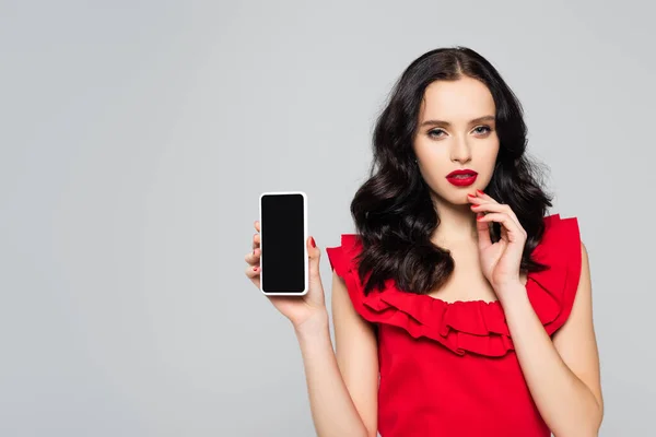 Mujer con labios rojos sosteniendo smartphone con pantalla en blanco aislado en gris - foto de stock