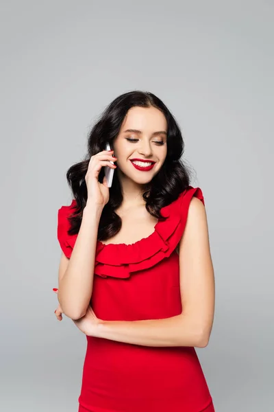 Весела жінка з червоними губами говорить на смартфоні ізольовано на сірому — стокове фото