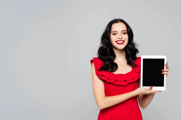 Mujer alegre con labios rojos sosteniendo tableta digital con pantalla en blanco aislada en gris — Stock Photo