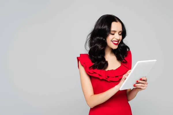 Cheerful woman with red lips using digital tablet isolated on grey — Stock Photo