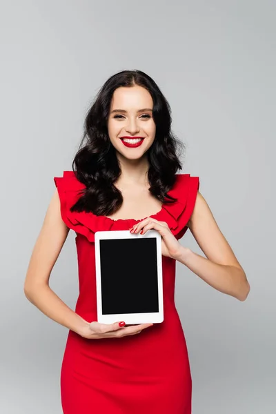 Mujer complacida con labios rojos sosteniendo tableta digital con pantalla en blanco aislada en gris - foto de stock