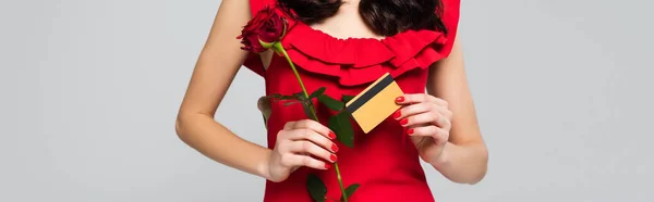 Vista recortada de la mujer sosteniendo rosa roja y tarjeta de crédito aislado en gris, bandera - foto de stock