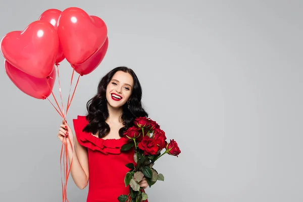 Щаслива жінка тримає червоні кулі у формі серця та троянди ізольовані на сірому — стокове фото
