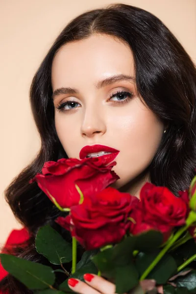 Morena joven con labios rojos sosteniendo rosas aisladas en rosa - foto de stock