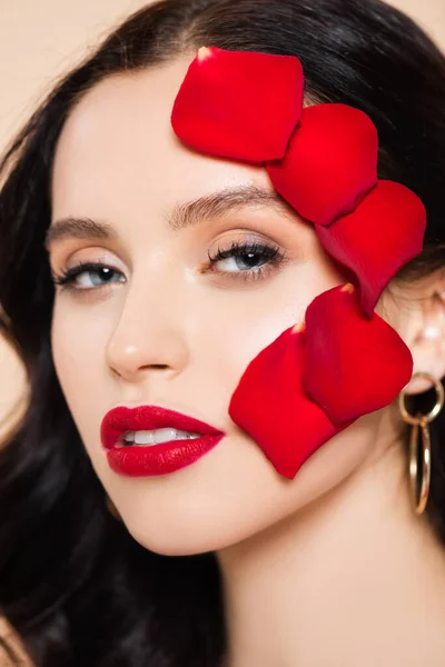 Primer plano de mujer joven con pétalos de rosa roja en la cara aislado en rosa - foto de stock