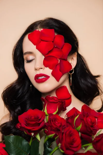 Jeune femme aux yeux fermés et pétales sur le visage près de roses isolées sur rose — Photo de stock
