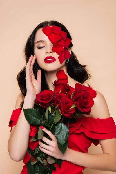 Brünette Frau mit geschlossenen Augen und Blütenblättern im Gesicht in der Nähe von Rosen isoliert auf rosa — Stockfoto