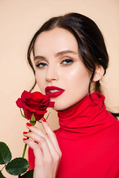 Femme sensuelle avec des lèvres rouges tenant rose rouge et regardant la caméra isolée sur rose — Photo de stock