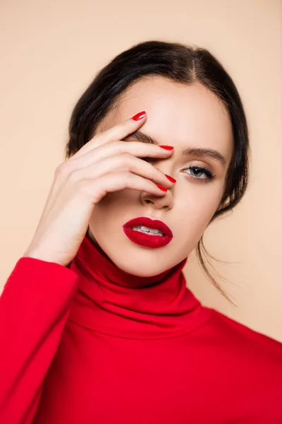 Brünette junge Frau mit roten Lippen, die Gesicht mit der Hand bedeckt und isoliert auf rosa Kamera schaut — Stockfoto