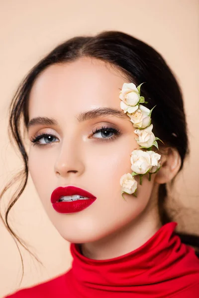 Femme avec des lèvres rouges et des fleurs sur le visage regardant la caméra isolée sur rose — Photo de stock