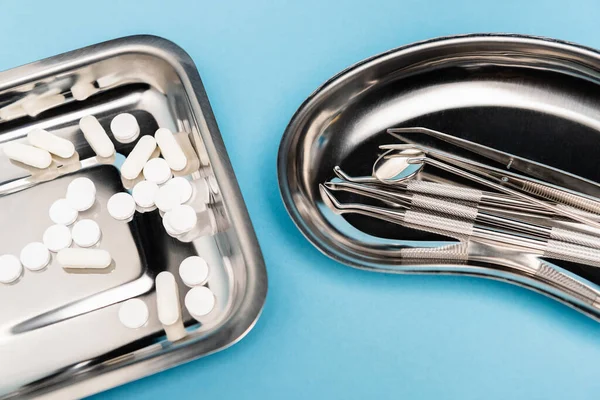 High angle view of pills and dental tools on trays on blue background — Stock Photo