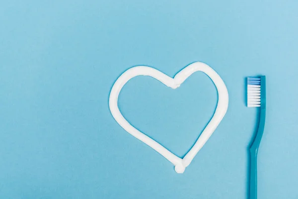 Вид сверху на знак сердца из зубной пасты и зубной щетки на синем фоне — стоковое фото