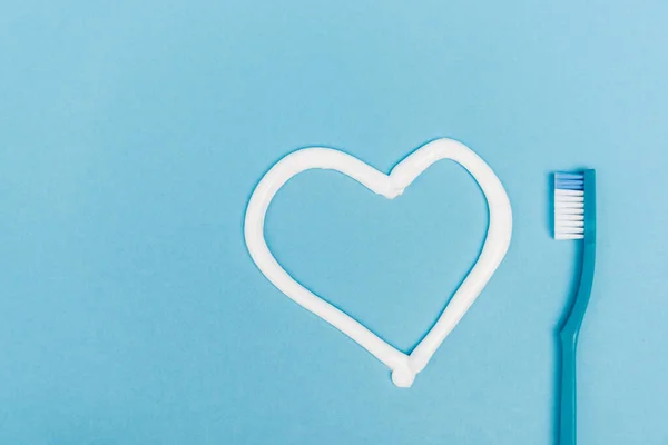 Vue du dessus du signe cardiaque du dentifrice et de la brosse à dents sur fond bleu — Photo de stock