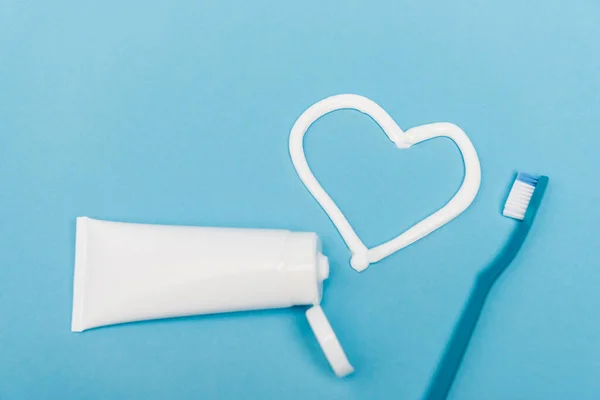 Vista dall'alto del tubo vicino al cuore da dentifricio e spazzolino da denti su sfondo blu — Foto stock