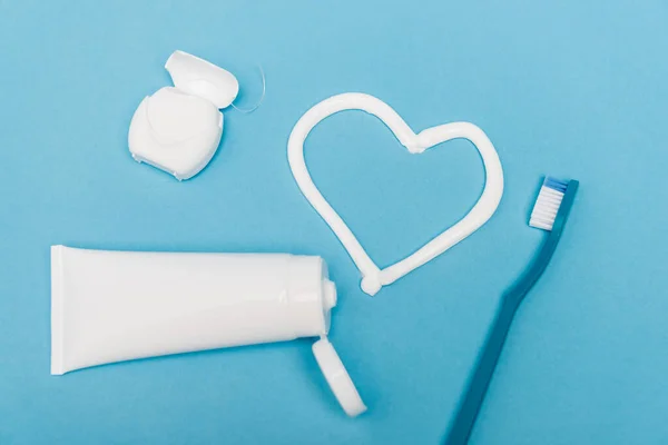 Vue du dessus du fil dentaire, de la brosse à dents et du signe cardiaque du dentifrice sur fond bleu — Photo de stock