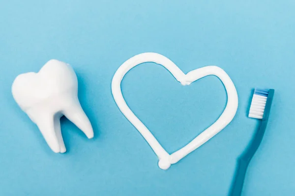 Vue du dessus du modèle de dent, signe cardiaque du dentifrice et de la brosse à dents sur fond bleu — Photo de stock