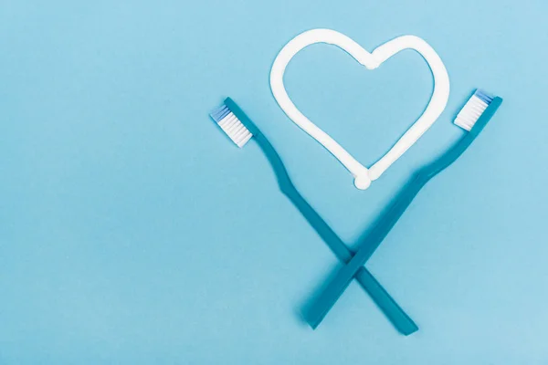 Vue du dessus des brosses à dents près du coeur signe du dentifrice sur fond bleu — Photo de stock