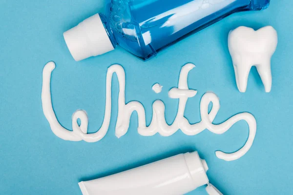 Top view of white lettering from toothpaste, tooth model and mouthwash on blue background — Stock Photo