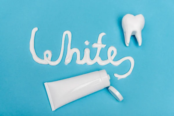 Top view of white lettering near tube of toothpaste and tooth model on blue background — Stock Photo