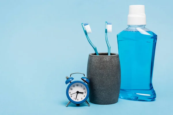 Toothbrushes near mouthwash and small alarm clock on blue background — Stock Photo