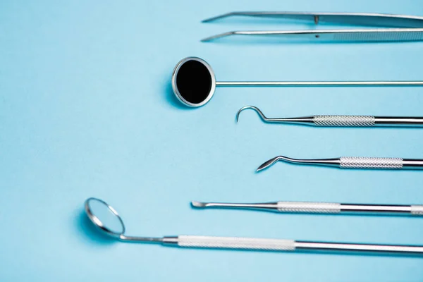 Vista de cerca del espejo dental y las herramientas en primer plano borroso sobre fondo azul - foto de stock