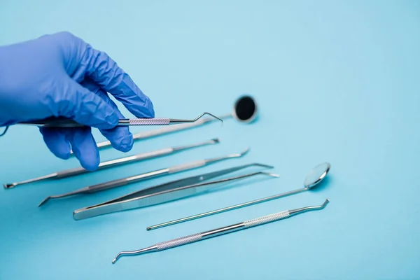 Cropped view of dentist holding tool near dental set blurred on blue background — Stock Photo