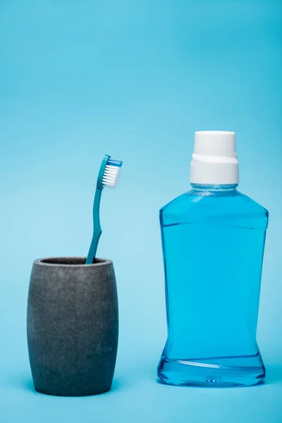 Bottle of mouthwash near toothbrush on blue background — Stock Photo