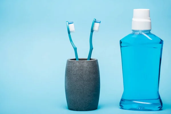 Cepillos de dientes y frasco de enjuague bucal oral sobre fondo azul - foto de stock