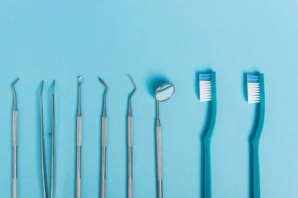 Vista superior de ferramentas dentárias inoxidáveis e escovas de dentes no fundo azul — Fotografia de Stock