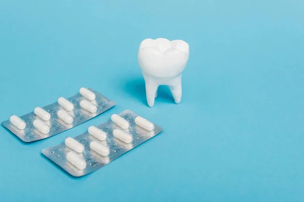 Vista de cerca de ampollas con pastillas y modelo de dientes sobre fondo azul - foto de stock