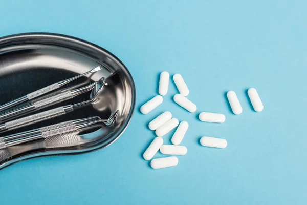 Закрыть обзор стоматологических инструментов в лотке и белых таблеток на синем фоне — стоковое фото