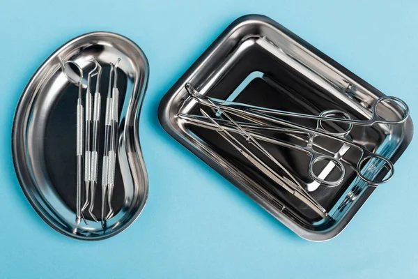 Vista superior de las herramientas dentales en bandejas de acero inoxidable sobre fondo azul - foto de stock