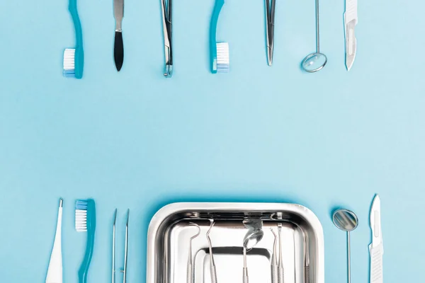 Vue du dessus des outils dentaires, plateau et brosses à dents sur fond bleu avec espace de copie — Photo de stock